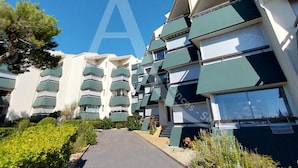A multi-story residential building with balconies, a clear sky, and a pathway leading to the entrance.