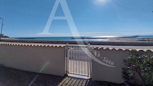 A balcony with a metal gate, overlooking a beach with a clear sky and sun.
