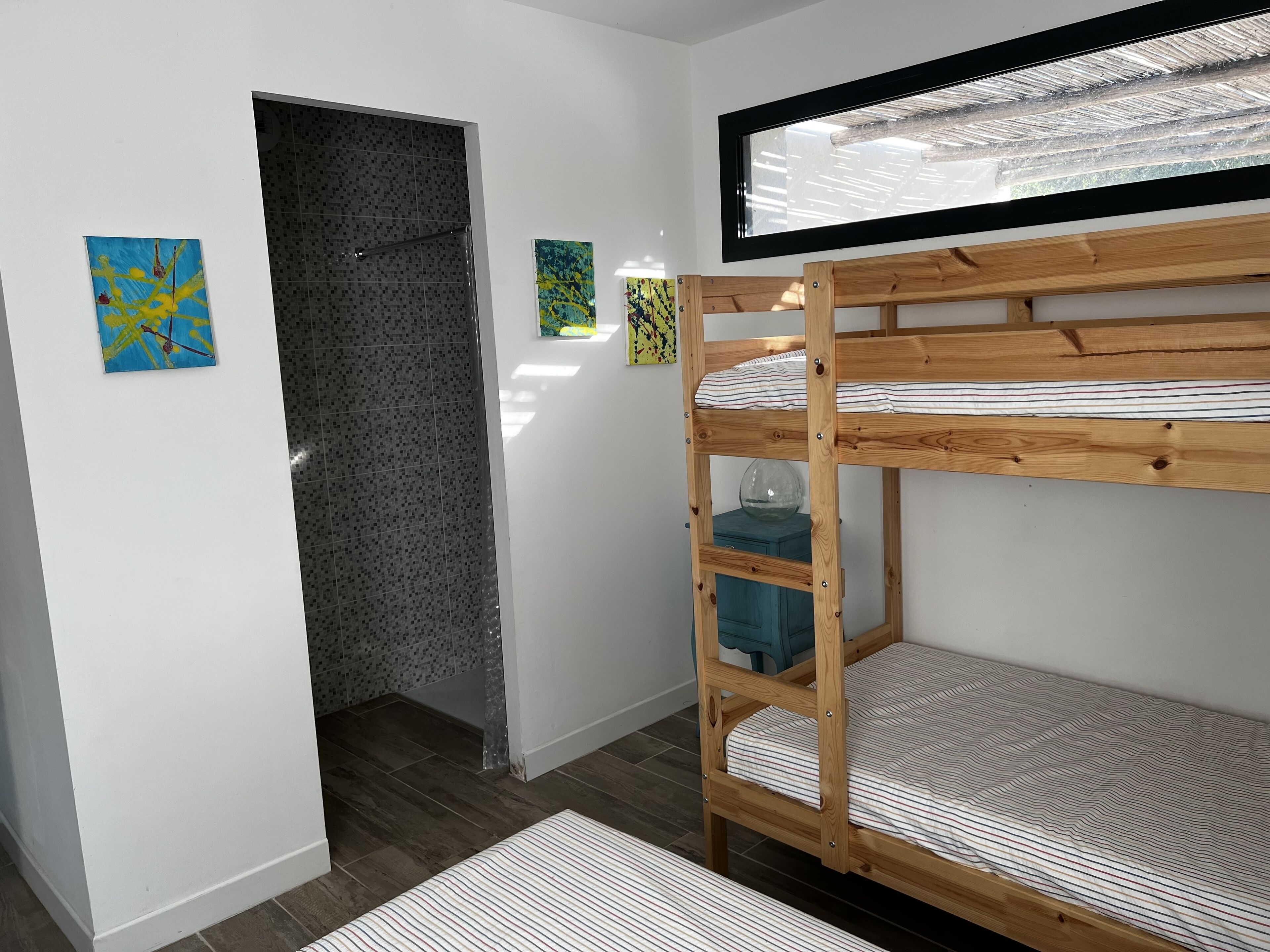 Una cama litera con estructura de madera, un mueble azul pequeño y dos cuadros en la pared.