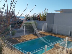 Piscina retangular com um deck de madeira, cercada por uma cerca branca.