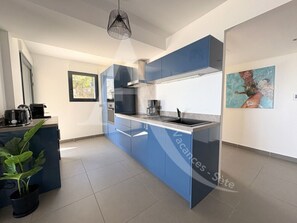 Uma cozinha moderna com armários azuis, uma ilha central, um lustre e um quadro na parede.