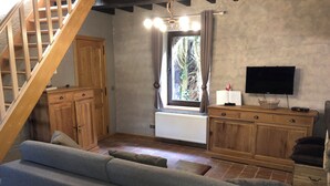 Un saló acollidor amb una escala de fusta, un sofà gris, armaris de fusta i una televisió.