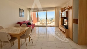 A spacious living area with a dining table, chairs, a red sofa, and a TV stand. - 2 CHAMBRES, LARGE TERRASSE, 1ERE LIGNE MER (Sète)