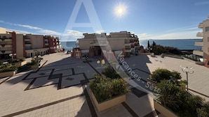 A spacious outdoor area with a clear view of the sea, featuring a modern building with multiple balconies and a central open space with seating areas. - 2 CHAMBRES, LARGE TERRASSE, 1ERE LIGNE MER (Sète)