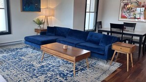 Un salon avec un canapé bleu, une table basse en bois et un coin repas comprenant une table et des chaises.