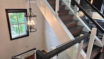 A modern staircase with glass railings and a wooden finish, leading to an upper level.