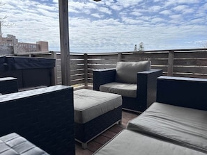 An outdoor patio with a wooden fence, a grill, and cushioned seating areas.