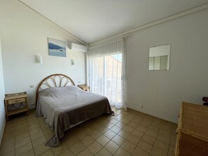 Um quarto com cama, mesa de cabeceira, cortinas em janela e ar condicionado fixado na parede.