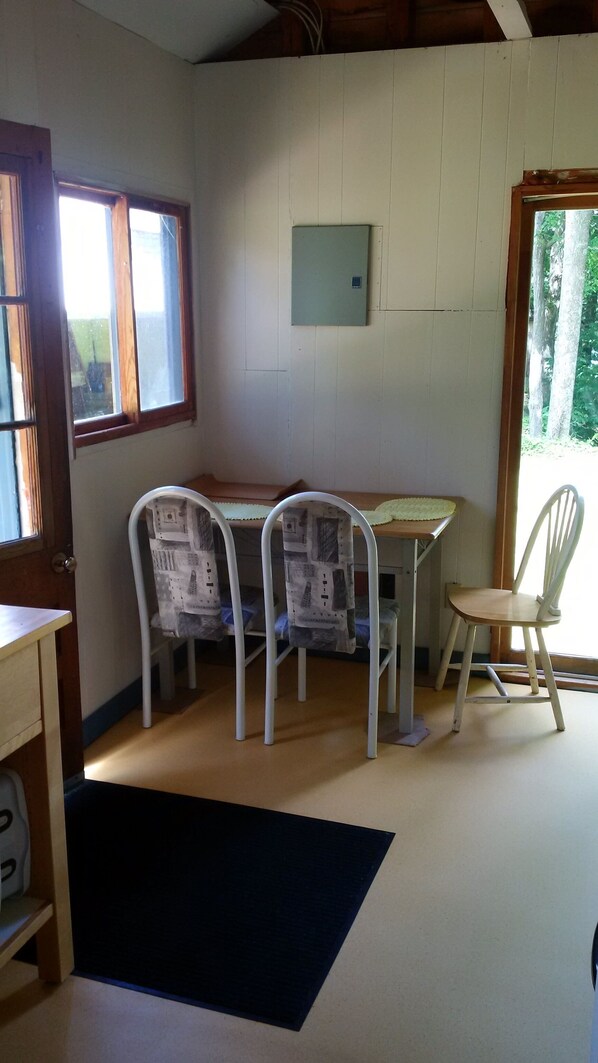 Ein Zimmer mit Holztisch, zwei Stühlen, einem Fenster und einer Tür.