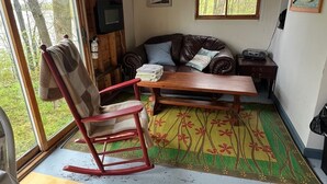 L’intérieur chaleureux d’un chalet avec un plafond en bois, un fauteuil à bascule, un canapé, une table et une vue magnifique par une grande fenêtre.