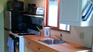 Une cuisine compacte équipée d’une cuisinière, d’un four à micro-ondes et d’un évier. Une fenêtre apporte de la lumière naturelle et un porte-ustensiles suspendu se trouve au-dessus de l’évier.