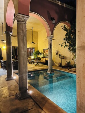 Zona de piscina con columnas, un área de descanso y una planta en maceta.