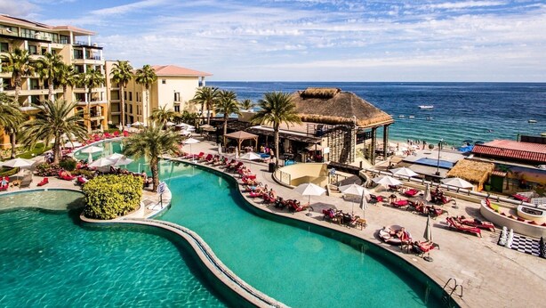 A resort with a large swimming pool, palm trees, and a beach area.