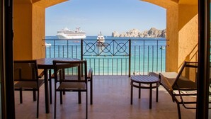 A balcony with a view of the sea, a cruise ship, and rocky cliffs.