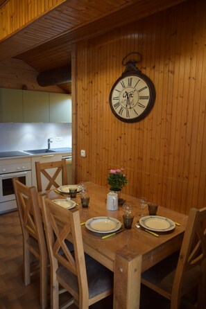 A wooden dining table with chairs, a wall-mounted clock, and a small potted plant.