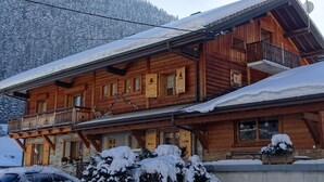 Un chalet en bois doté d’un balcon, entouré d’arbres et de montagnes couverts de neige.