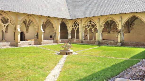 Une cour intérieure avec une fontaine centrale, entourée de passages voûtés et bordée d’un bâtiment doté d’un toit en tuiles.