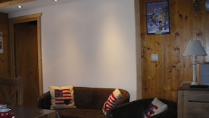 Un salon chaleureux avec un canapé en cuir marron, deux coussins à rayures rouges et blanches, un mur en bois et un tableau encadré.