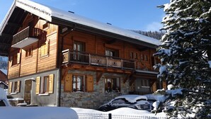 Un chalet en bois doté d’un balcon, avec des fondations en pierre et entouré d’un paysage enneigé.