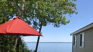 A picnic setup with a table and chairs, a red umbrella, and a view of the water. - TWO Waterfront Camps on Sebago Lake (Standish)