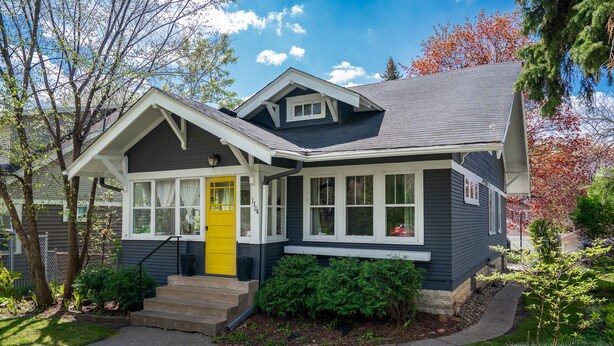Une maison à deux étages avec une porte d’entrée jaune, des moulures blanches et un porche abrité.