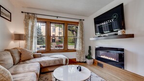 Un salon comprenant un canapé, une table basse, une cheminée et un téléviseur fixé au mur.