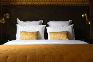 Ein Bett mit Kissen in Weiß und Gelb mit Muster, ein Holzkopfschild und Wandleuchten aus Gold.