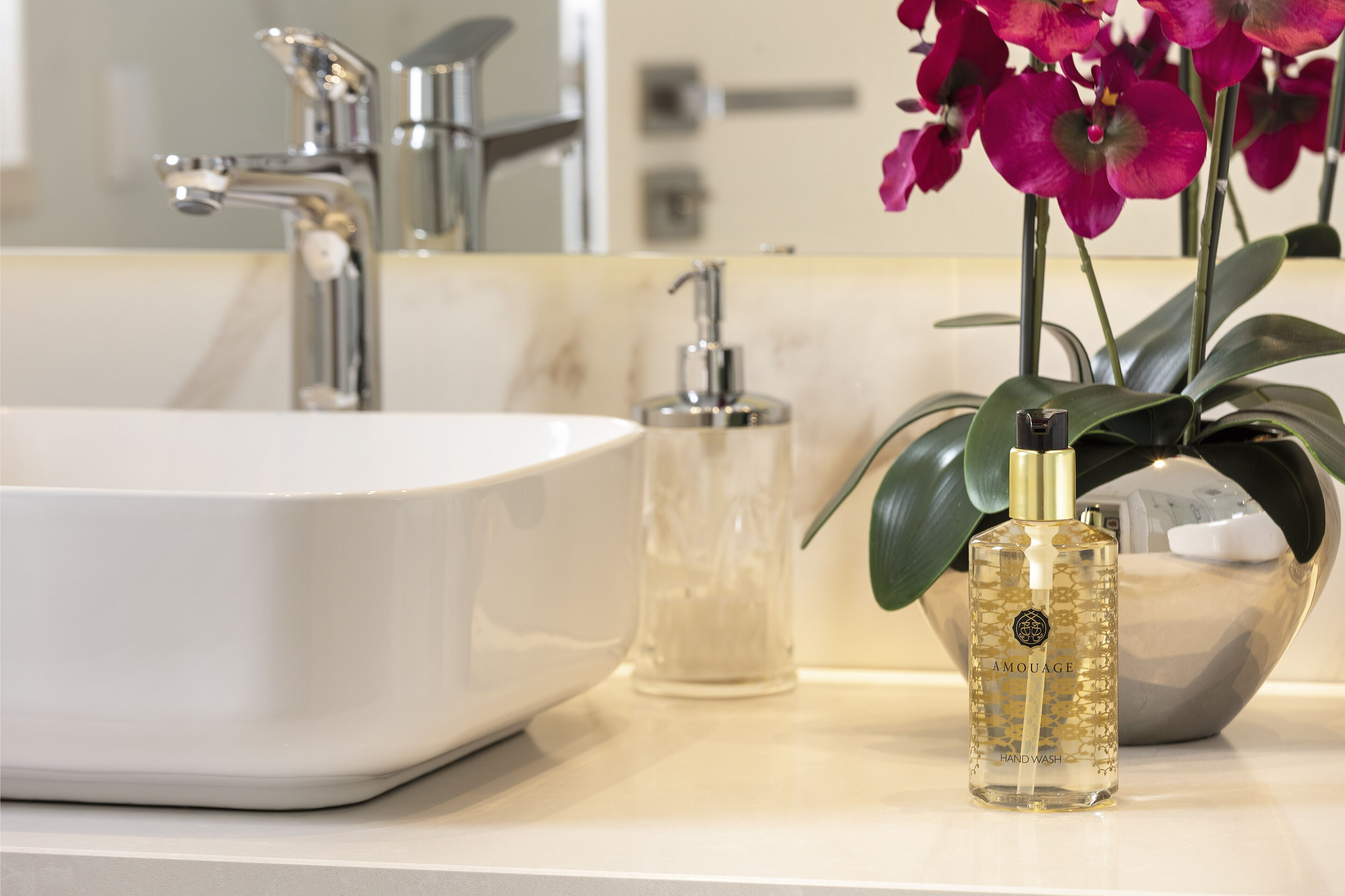 A bathroom sink, a hand soap dispenser, and a bottle of handwash.