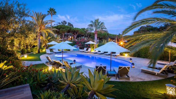A swimming pool surrounded by lounge chairs and umbrellas, with palm trees and well-maintained landscaping. - Vila Balaia - Luxury Boutique Villas (Albufeira)