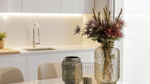 A modern kitchen with white cabinets, a stainless steel faucet, a glass vase with flowers, and a decorative metal container on the counter. - Vila Balaia - Luxury Boutique Villas (Albufeira)