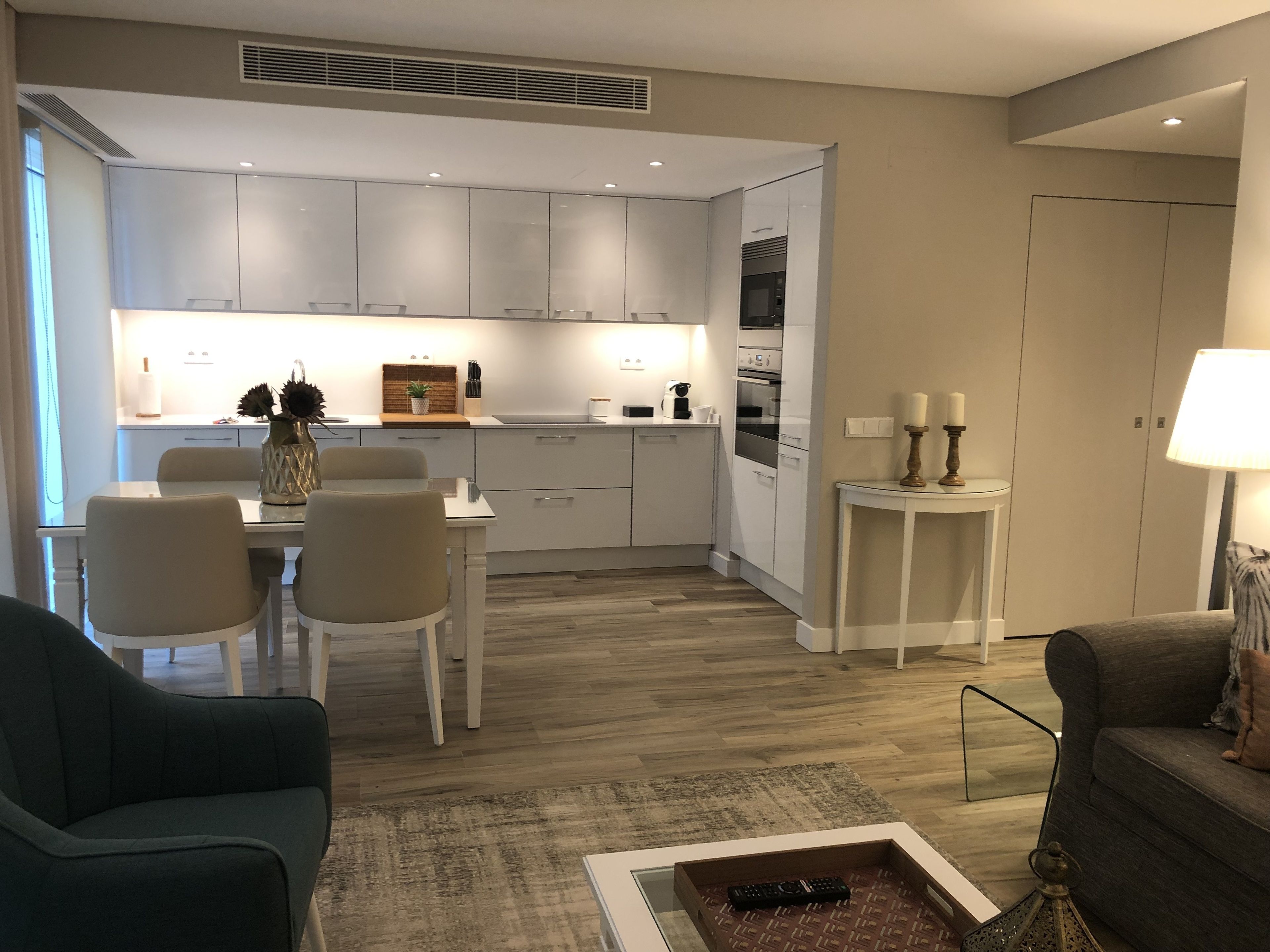A modern kitchen with white cabinets, a dining area with a table and chairs, and a living area with a sofa and a coffee table.