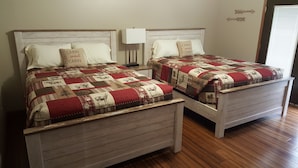 Deux lits en bois, assortis, avec des têtes de lit et des pieds de lit identiques, chacun étant agrémenté d’une table de chevet blanche et d’une lampe.