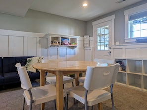 A room with a round wooden table, white chairs, a dark blue sofa, and white shelving units with books and toys.