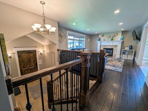 Un intérieur spacieux avec un escalier en bois, une cheminée et une vue sur l’extérieur.