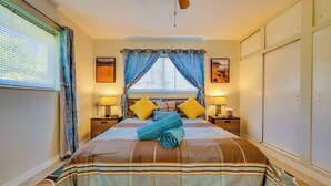 Une chambre bien rangée, avec un lit, deux tables de chevet, un ventilateur de plafond et une fenêtre avec des rideaux.