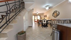 A spacious kitchen with a dining area, a staircase, and a trash bin. - Casa de Pauline - Noord (Noord)