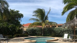 A clear blue pool with lounge chairs and palm trees. - Casa de Pauline - Noord (Noord)