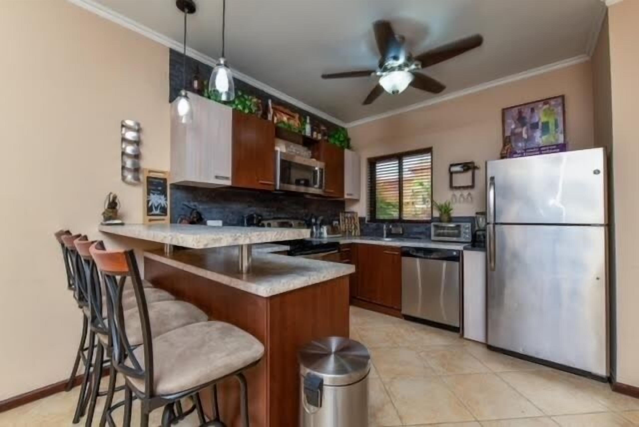 Une cuisine dotée d’un îlot central, de tabourets de bar, d’un réfrigérateur en acier inoxydable et d’un ventilateur de plafond.