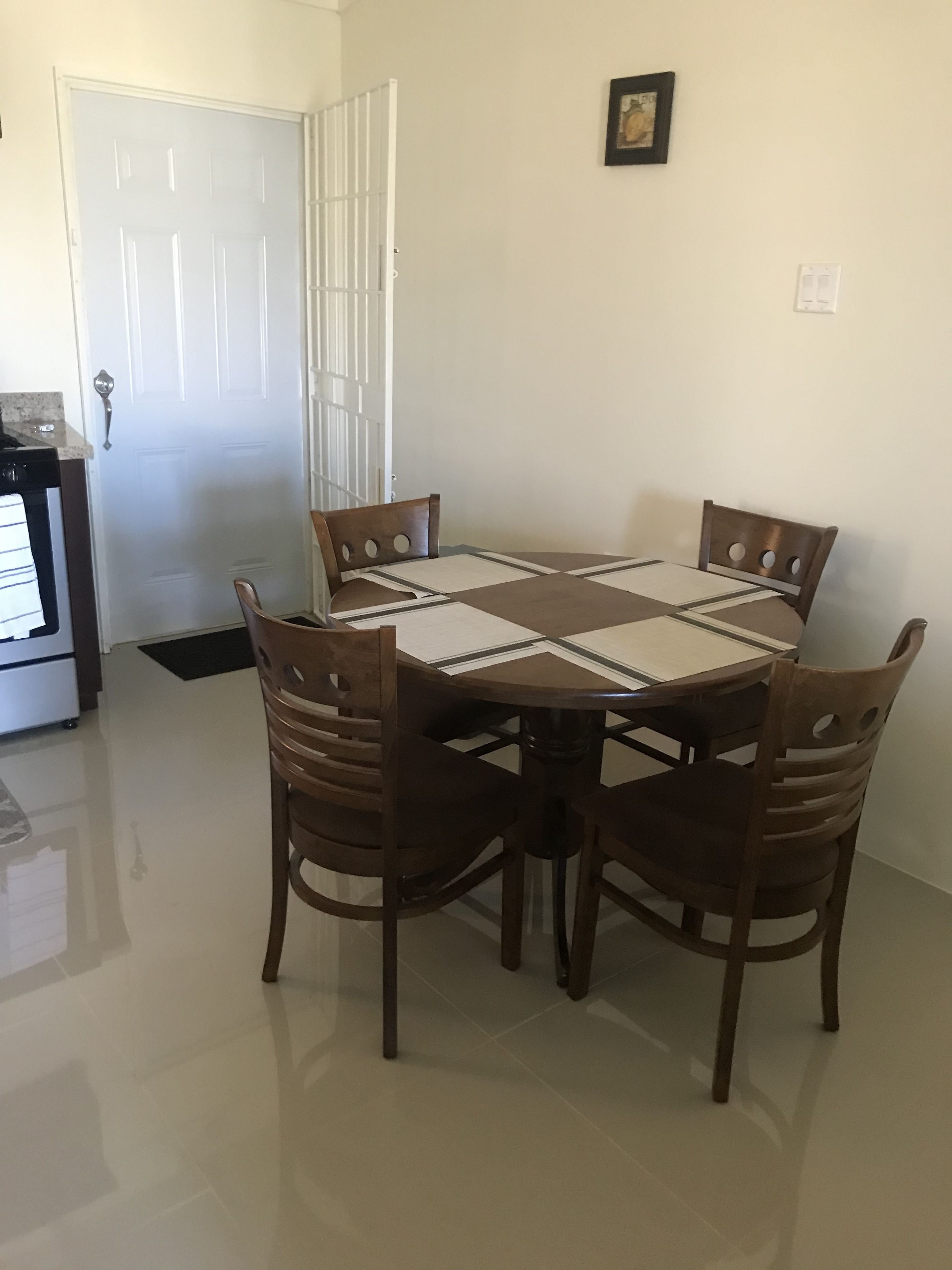 A dining area with a round table and four chairs, a white door, and a small picture on the wall.