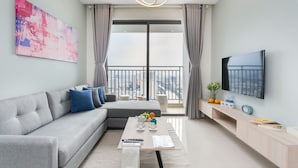 A modern living room with a grey sofa, a coffee table, a flat-screen TV, and a balcony with a city view. - The Grand Saigon Apartment - City Centre (Ho Chi Minh City)