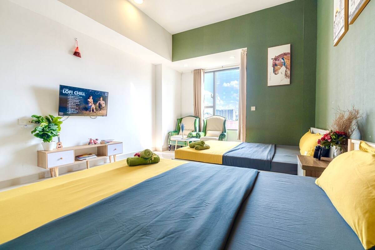 Ein Hotelzimmer mit zwei Betten, einem Fernseher an der Wand, einem Fenster mit Aussicht und einem kleinen Tisch mit Stuhl.