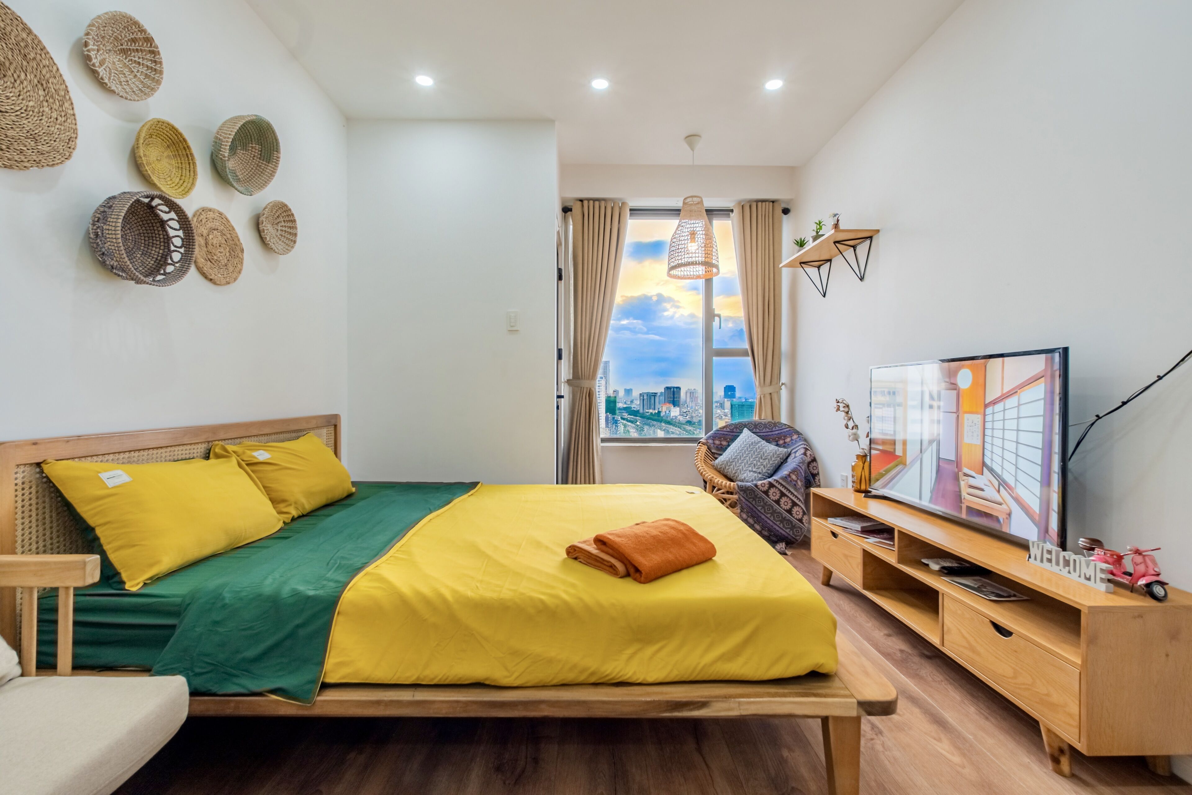 Una habitación de hotel moderna con una cama grande, un banco de madera, televisión y vistas a la ciudad.