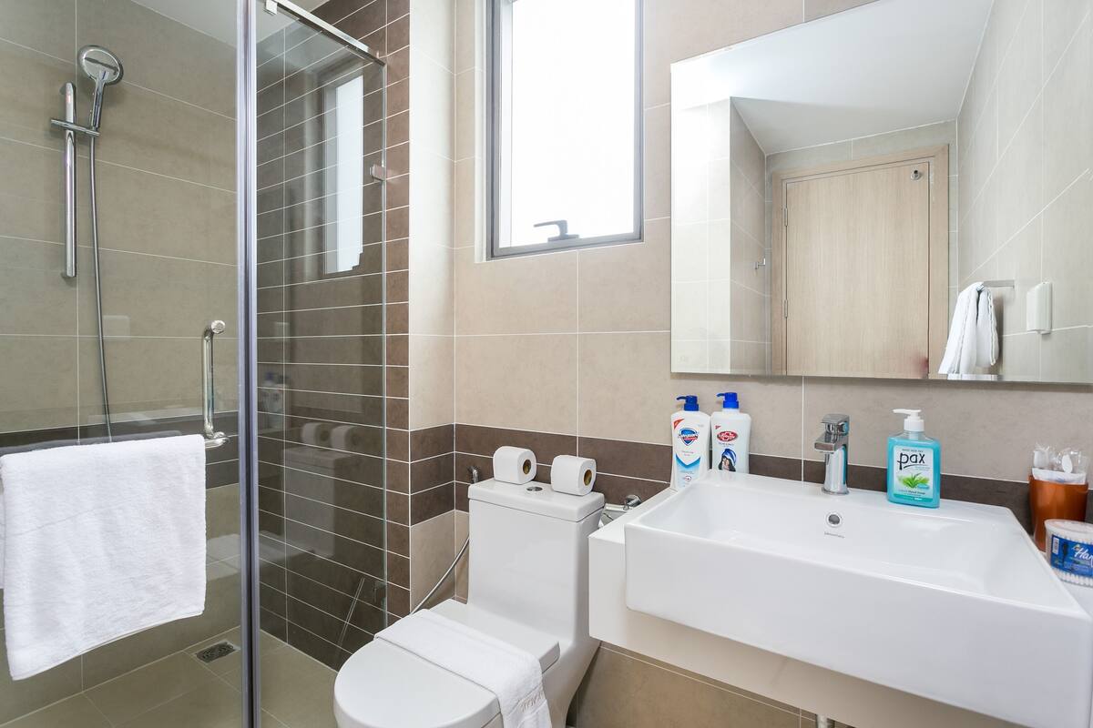 Ein Badezimmer mit Duschkabine aus Glas, Toilette, Waschbecken mit Spiegel und Pflegeprodukten auf der Ablagefläche.
