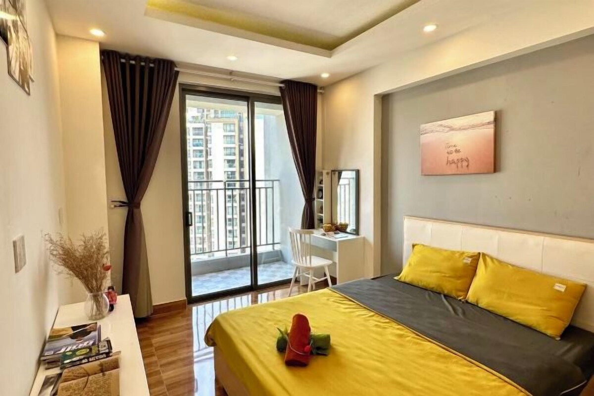 A hotel room with a bed, a desk, and a view of the city through large windows.