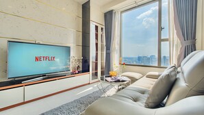 A modern living room with a large flat-screen TV displaying 'NETFLIX', a leather sofa, a glass coffee table, and a view of the city through a large window. - The Grand Saigon Apartment - City Centre (Ho Chi Minh City)