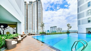 A modern rooftop pool area with a clear blue pool, wooden deck, and wicker lounge chairs. - The Grand Saigon Apartment - City Centre (Ho Chi Minh City)