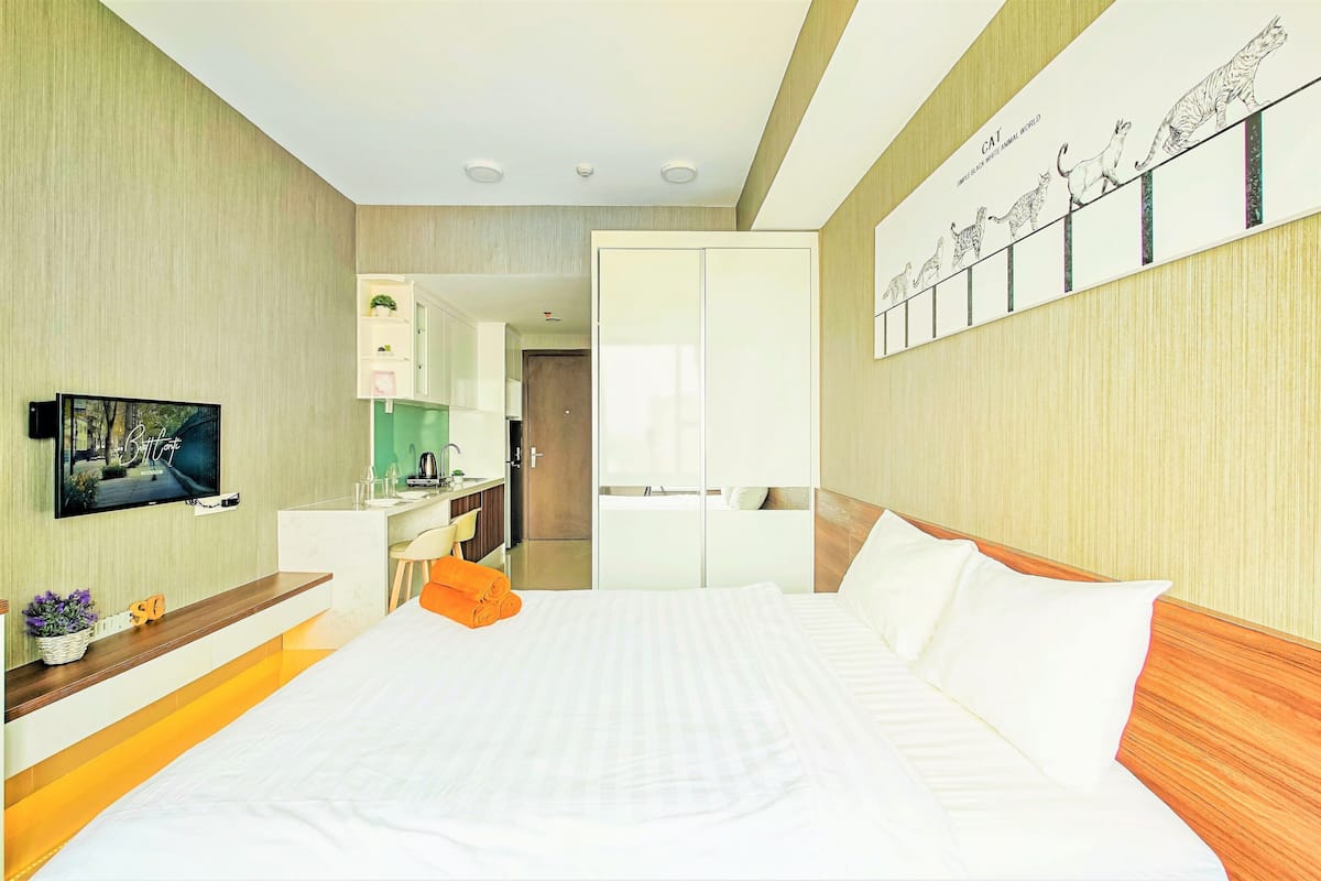 Ein Hotelzimmer mit Bett, Fernseher, Schreibtisch und einer Küchenzeile.