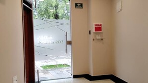 Un pasillo con piso de baldosas, una puerta que da al exterior y un letrero que indica una salida de emergencia.