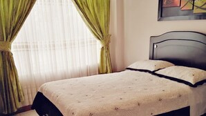 Una cama con cubrecama acolchado, cabecera y cortinas.