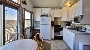 A kitchen with white cabinets, a refrigerator, a stove, and a microwave. There is a window with curtains and a view of the outside. - Ocean's Door East is fun for the whole family! (HATTERAS)